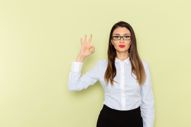 Front view of female office worker in white shirt and black skirt smiling on green wall