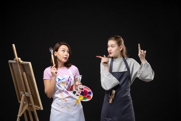 正面図女性画家がイーゼルで他の女性と一緒に黒い壁に絵を描く写真カラーアート写真アーティストが仕事を描く
