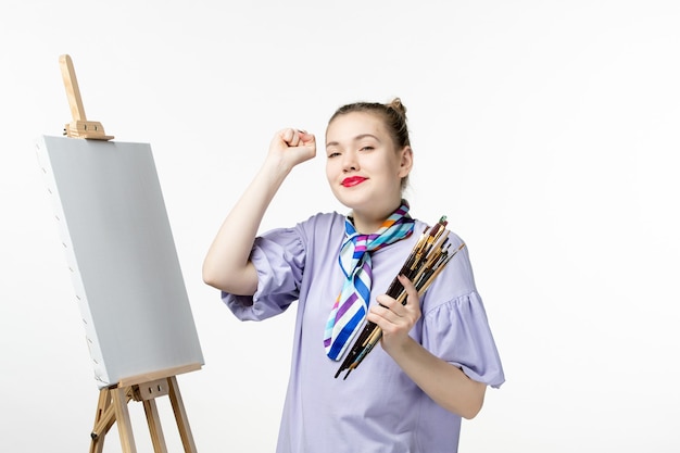 Front view female painter holding tassels for drawing on the white wall woman picture art photo paint draw artist pencil easel