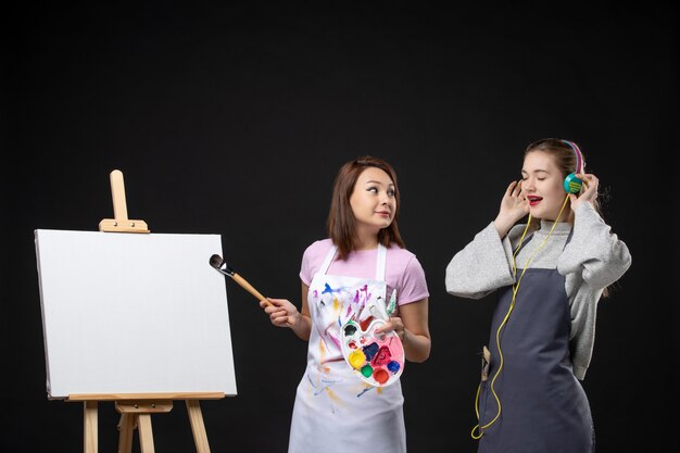 front view female painters one draws and other is listening to music on black wall artist job photo draw painting art picture color