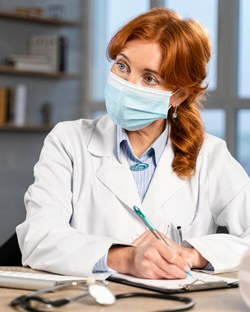 Front view of female physician with medical mask at her desk writing prescription