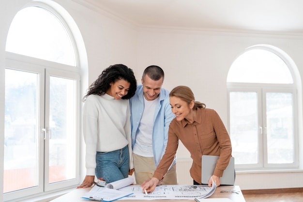 Front view of female realtor showing new house plan to couple