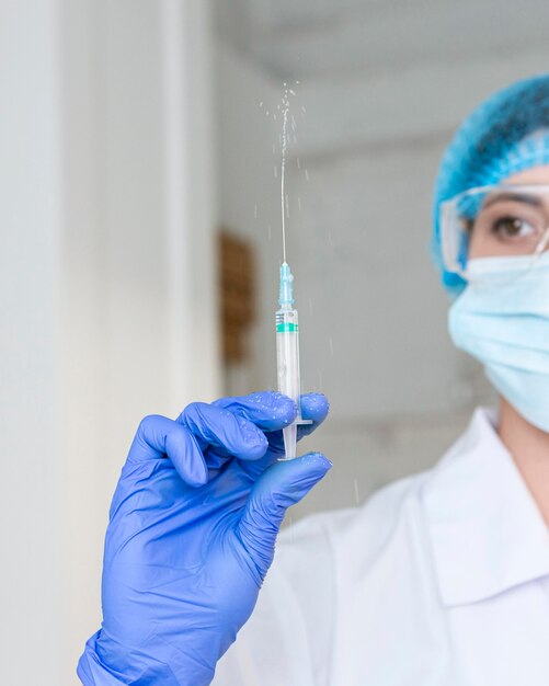 Front view of female researcher with safety glasses and gloves holding syringe