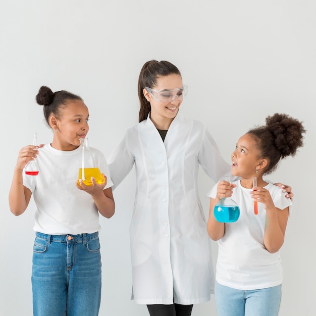 Vista frontale della scienziata che posa con le ragazze che tengono pozioni in tubi