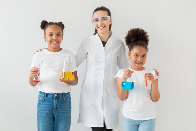 Front view of female scientist posing with young girls holding test tubes