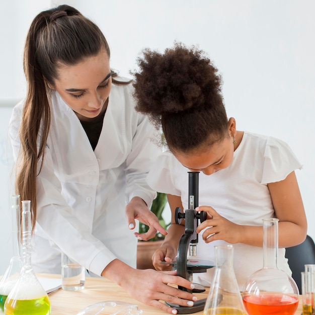 Free photo front view of female scientist teaching girl to look through microscope