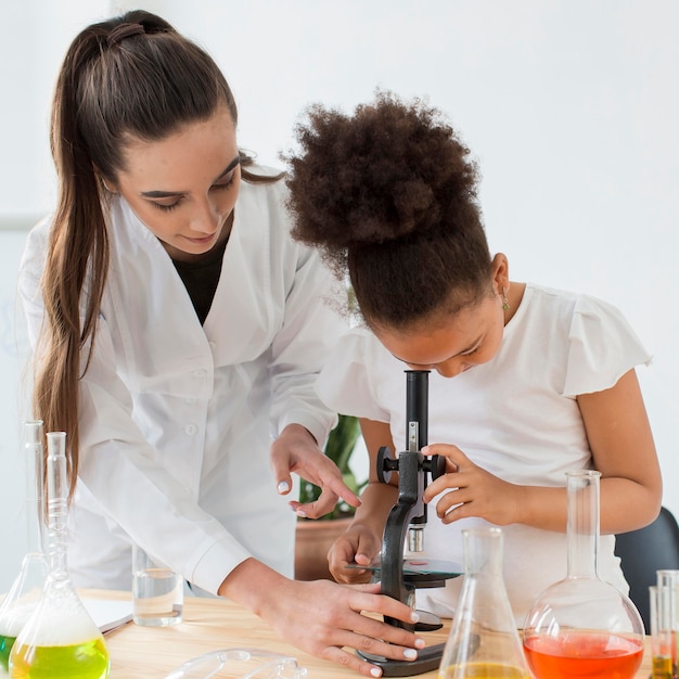 Front view of female scientist teaching girl to look through microscope