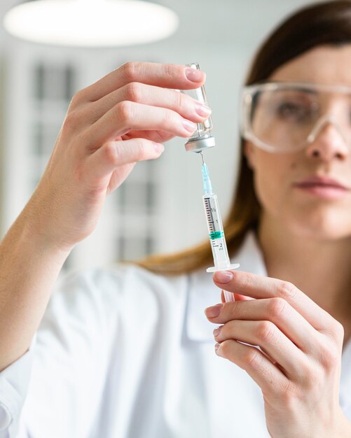 Front view of female scientist with safety glasses holding syringe with vaccine