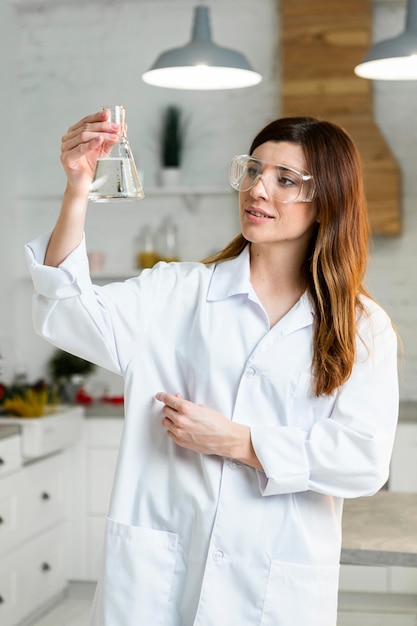 Вид спереди ученого в защитных очках, держащего пробирку в лаборатории