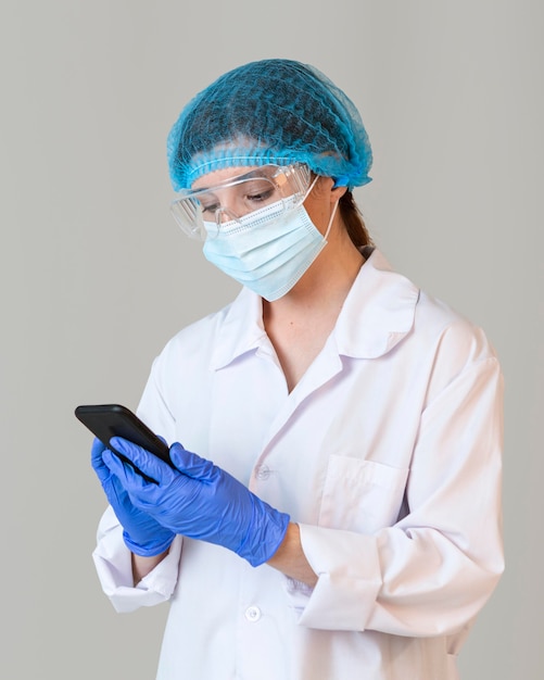 Front view of female scientist with safety glasses and medical mask holding smartphone
