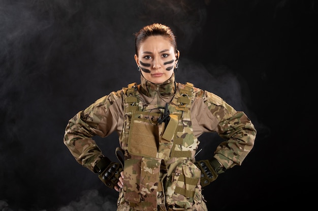 Женщина-солдат в камуфляже на темной стене, вид спереди