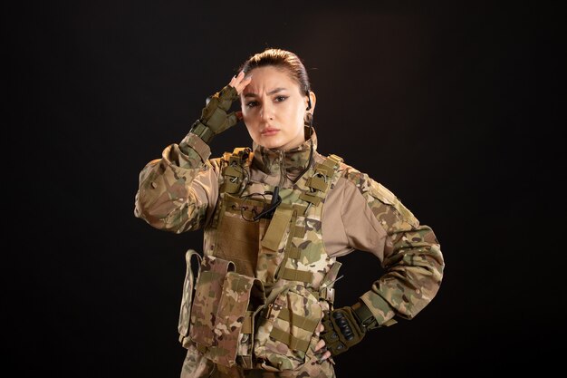 검은 벽에 두통이 있는 위장을 한 여성 군인의 전면 모습