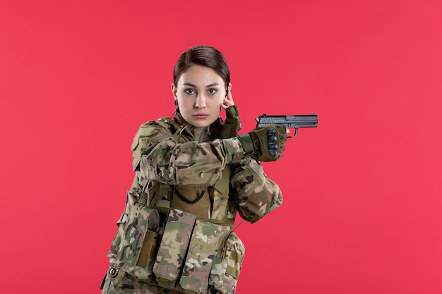 Front view of female soldier in camouflage holding gun on red wall