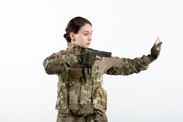 Soldato femminile di vista frontale in camuffamento con la pistola sulla parete bianca