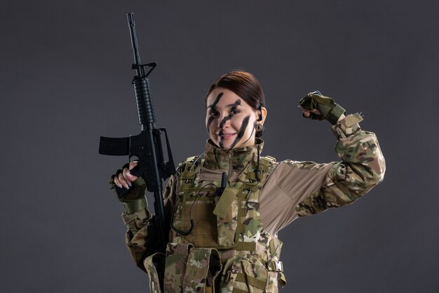 Front view female soldier in camouflage with machine gun on a dark wall