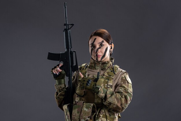 Front view of female soldier in camouflage with machine gun on a dark wall