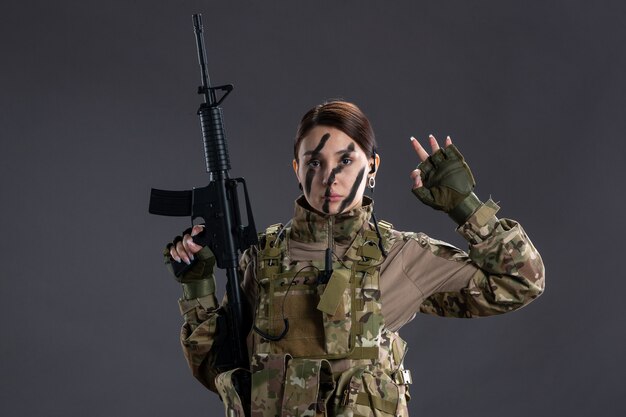 Вид спереди женщина-солдат в камуфляже с пулеметом на темной стене
