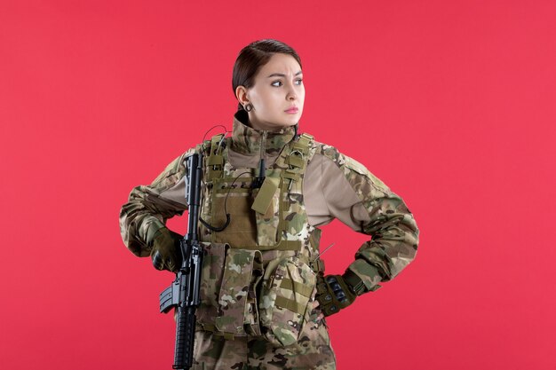 Front view female soldier in camouflage with machine gun on red wall