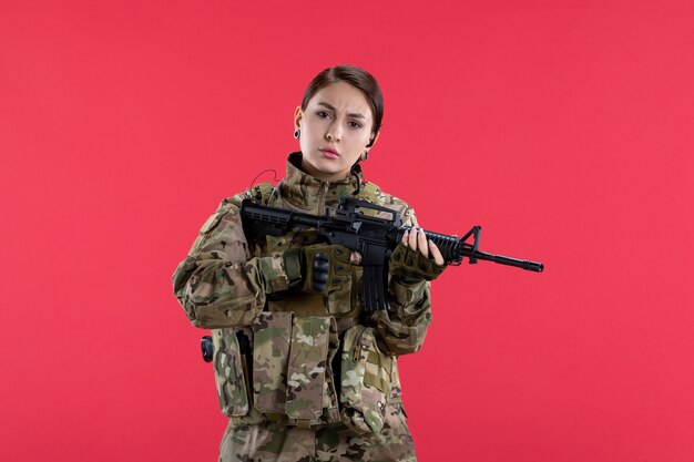 Front view female soldier in camouflage with machine gun on red wall