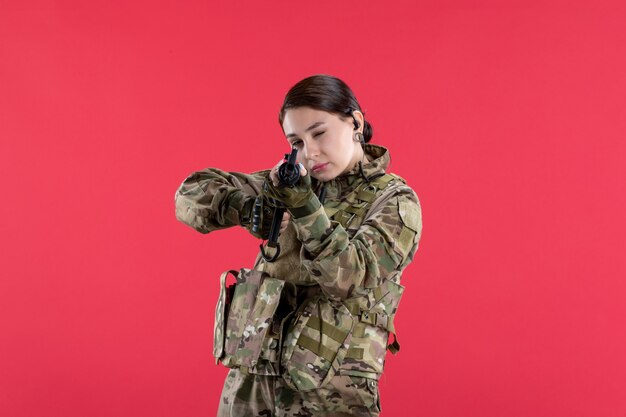 Вид спереди женщина-солдат в камуфляже с пулеметом на красной стене