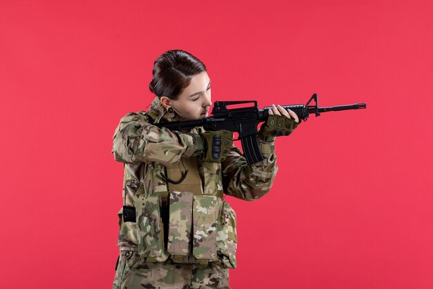 Front view of female soldier in camouflage with machine gun on red wall