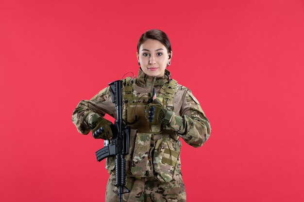 Вид спереди женщина-солдат в военной форме с пулеметом на красной стене