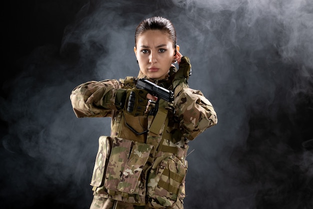 Foto gratuita soldato femminile di vista frontale in uniforme con la pistola sulla parete nera