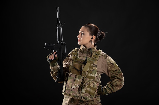 Front view of female soldier in uniform with rifle on a black wall