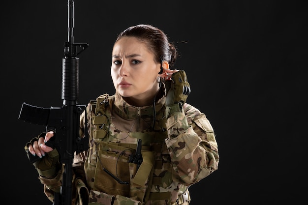 Vista frontale della soldatessa in uniforme con il fucile sul muro nero