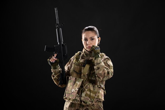 Front view of female soldier in uniform with rifle on black wall