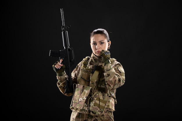 Front view of female soldier in uniform with rifle on black wall