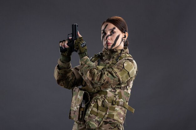 Front view of female soldier with gun in camouflage dark wall