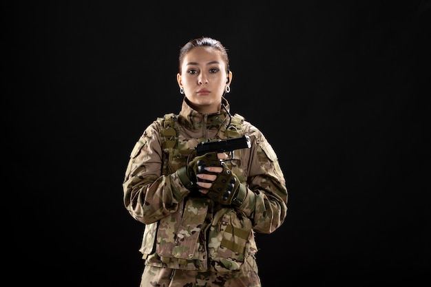 Front view female soldier with gun in uniform on a black wall