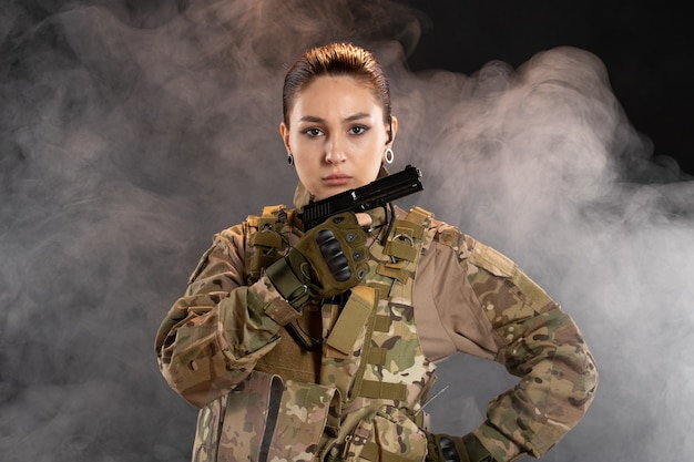 Foto gratuita vista frontale della soldatessa con la pistola in uniforme sul muro nero