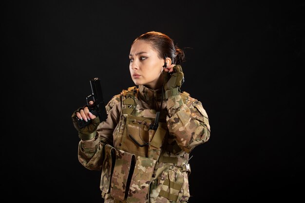 Front view of female soldier with gun in uniform on black wall