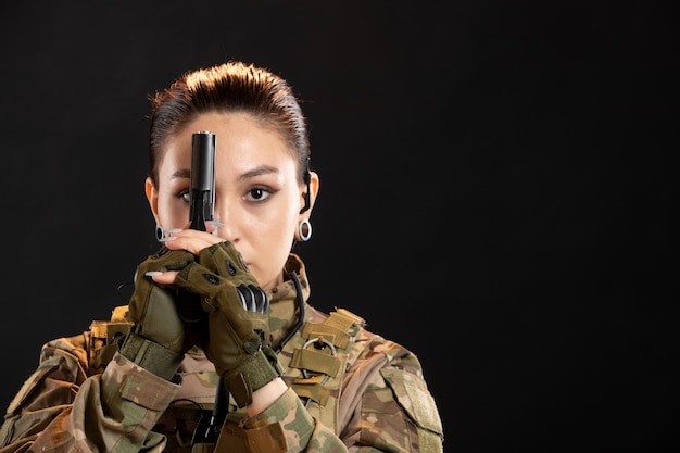 Front view of female soldier with gun in uniform on black wall