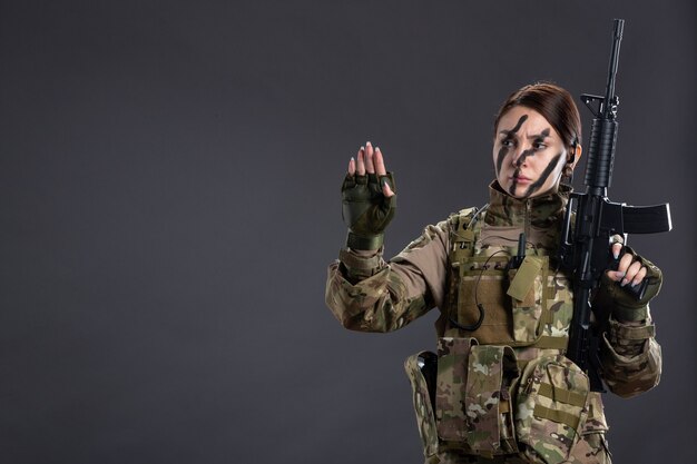 Front view female soldier with machine gun in camouflage dark wall