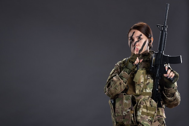 Front view female soldier with machine gun in camouflage dark wall