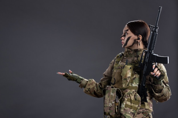 Foto gratuita soldato femminile di vista frontale con la mitragliatrice in camuffamento sulla parete scura