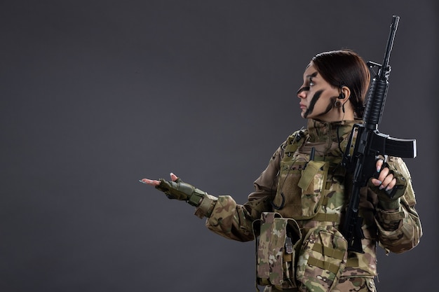 Front view female soldier with machine gun in camouflage dark wall