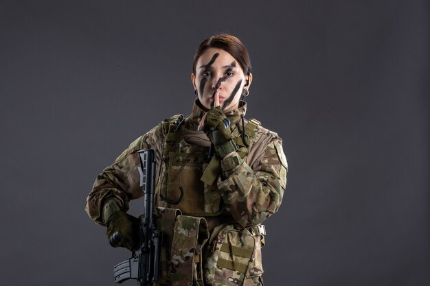 Вид спереди женщина-солдат с пулеметом в камуфляже на серой стене