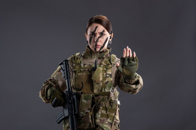 Front view female soldier with machine gun in camouflage on gray wall