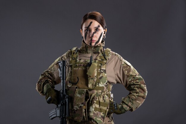 회색 벽에 위장에 기관총을 가진 전면 보기 여성 군인