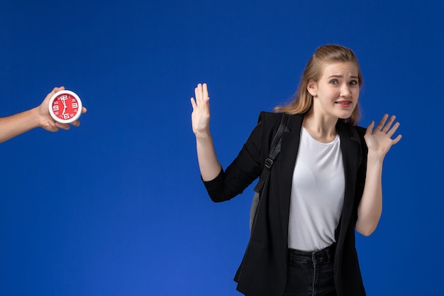 Foto gratuita studentessa di vista frontale in giacca nera che indossa uno zaino sul muro blu scuola college università lezione tempo