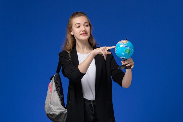 Front view female student in black jacket wearing backpack holding little globe on the blue wall school college university lessons earth