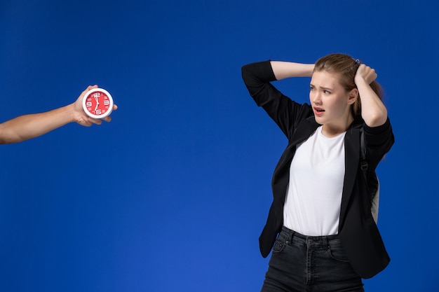 Front view female student in black jacket wearing backpack on light-blue wall school college university lessons time