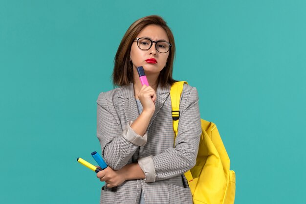 밝은 파란색 벽에 생각하는 펠트 펜을 들고 그녀의 노란색 배낭을 착용하는 회색 재킷에 여성 학생의 전면보기