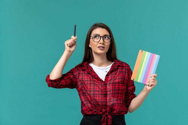 Front view of female student holding copybook and pen on the blue wall