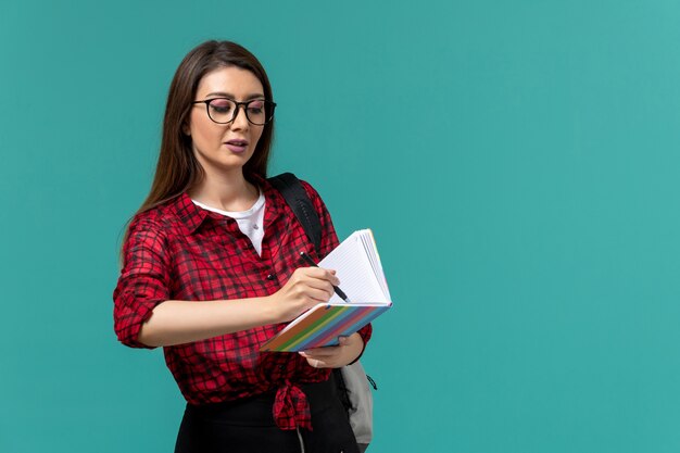 Front view of female student holding copybook and pen writing on blue wall