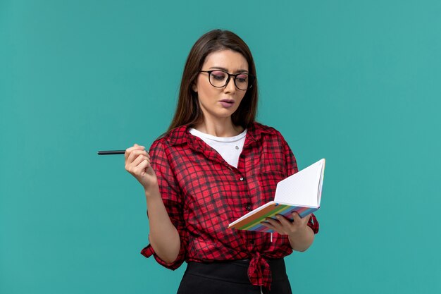 Front view of female student holding copybook and pen writing on the blue wall